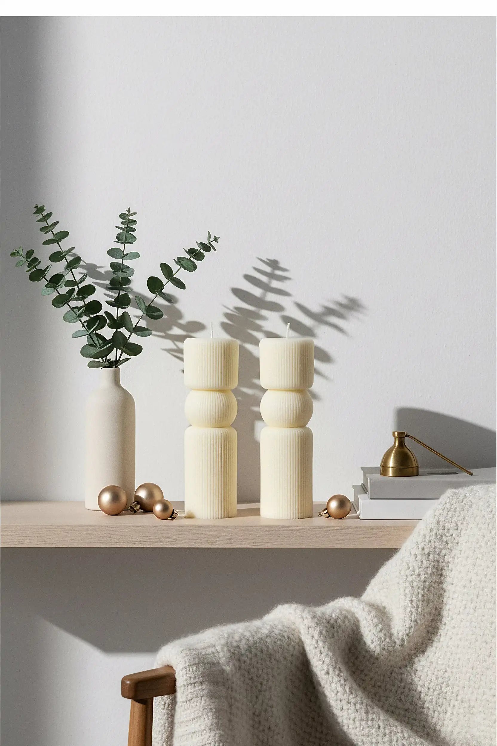 Decorative setup with vases, pillar candles, and a plant on a table against a light gray wall.